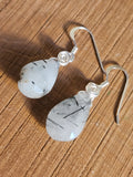 Silver earrings with teardrop-shaped stones on a wooden surface