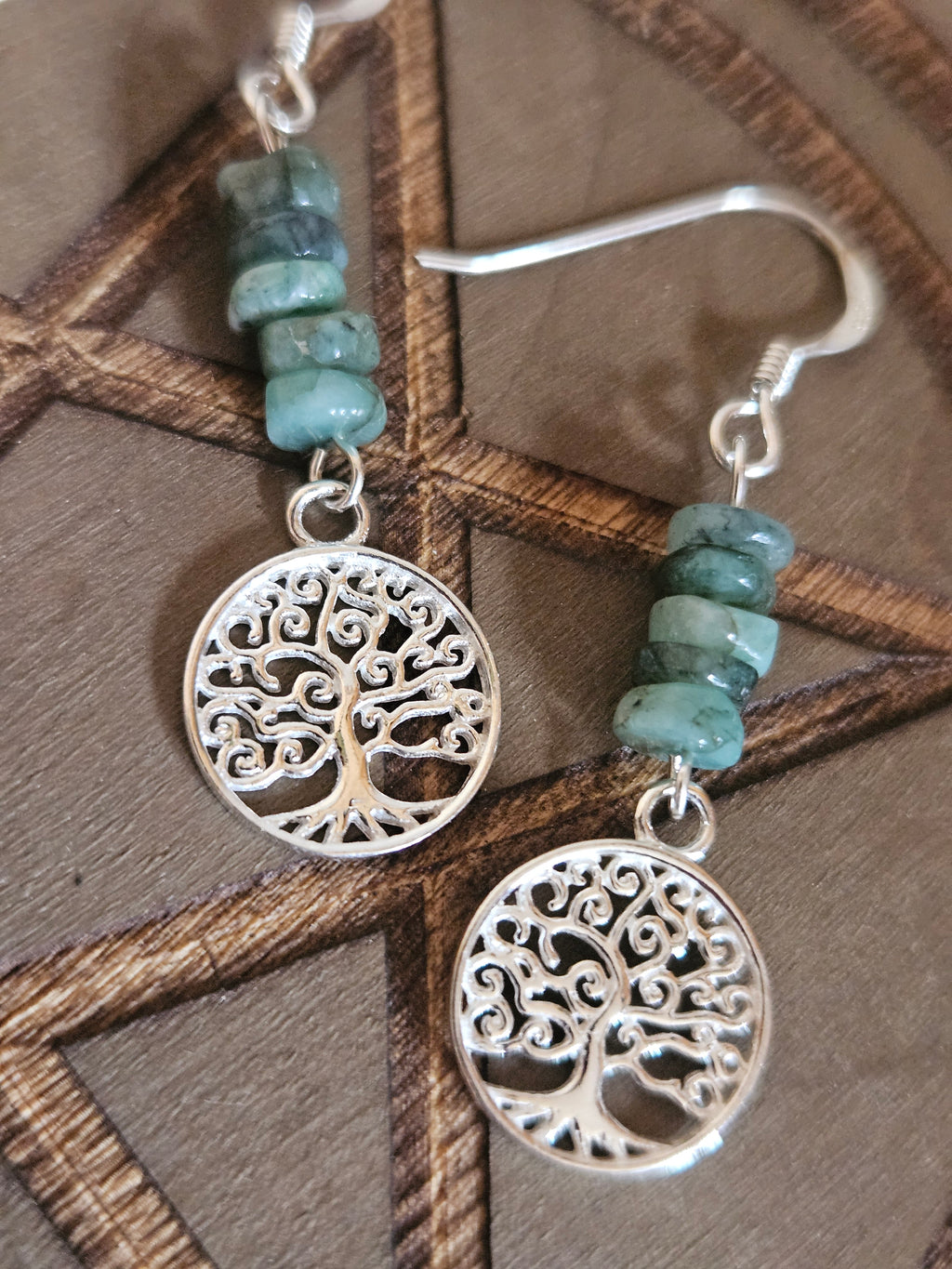 Silver earrings with tree of life design and turquoise beads on a wooden surface