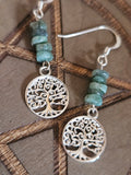 Silver earrings with tree of life design and turquoise beads on a wooden surface