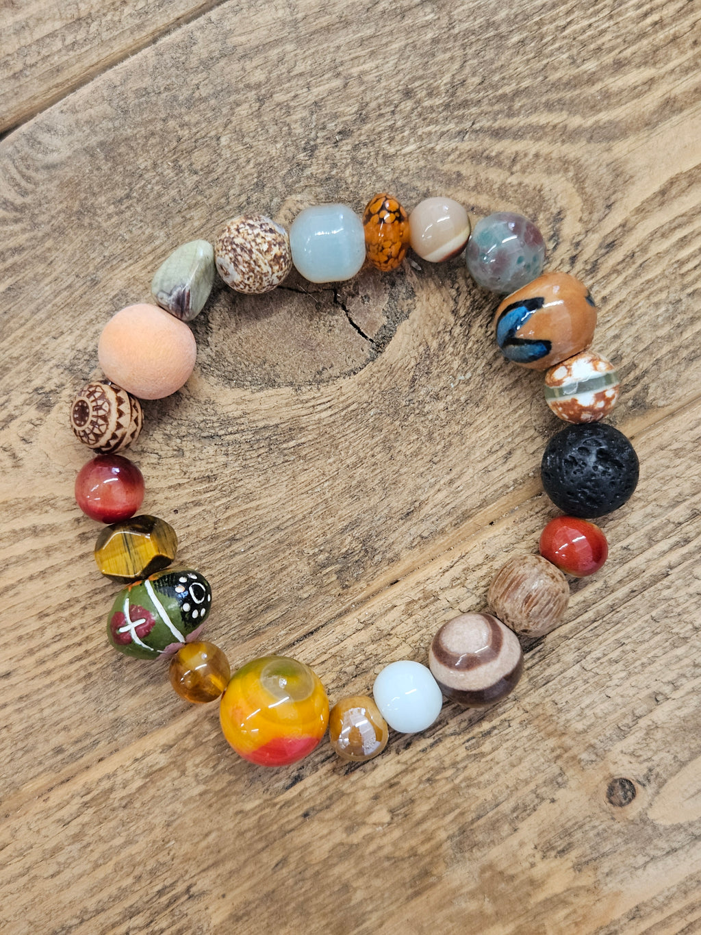 A beaded stretch bracelet made of various colorful, patterned, and textured glass beads, displayed on a rustic wooden surface.