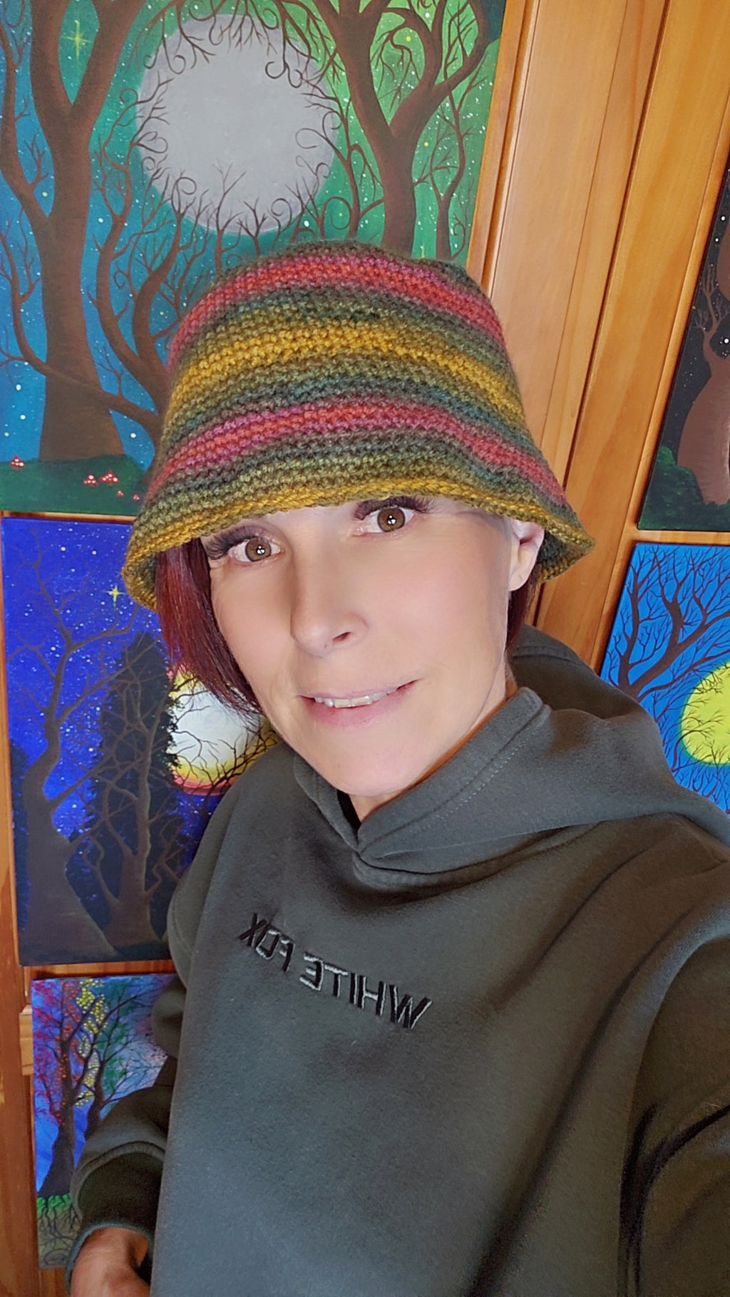 Person wearing a colorful crochet hat in front of a artwork 