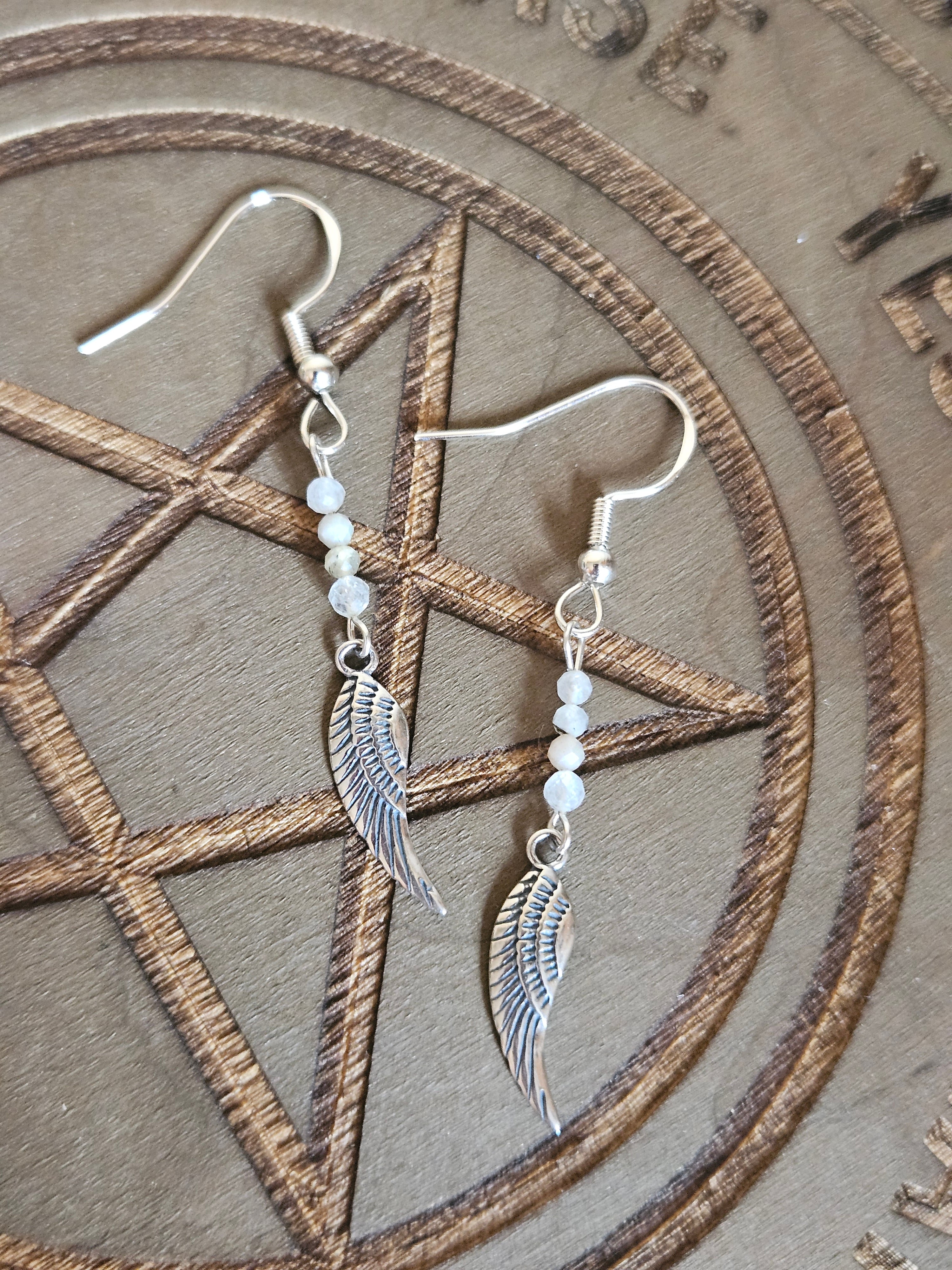 Silver wing-shaped earrings with beads on a pentagram design background