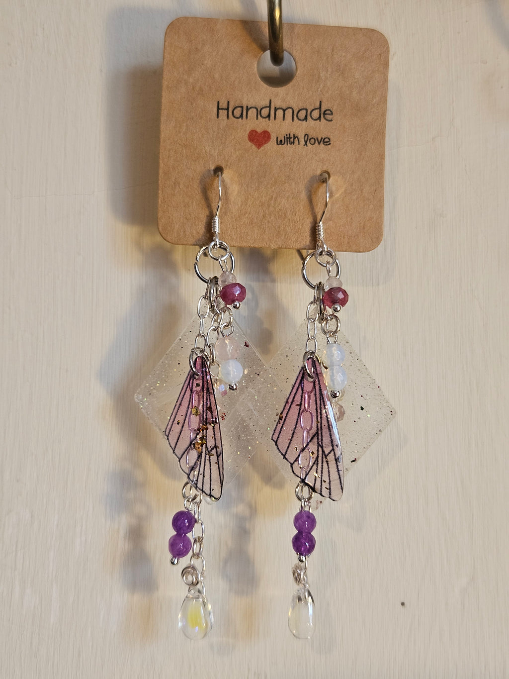 Pair of decorative earrings on a clear stand with a 'Handmade with Love' tag.