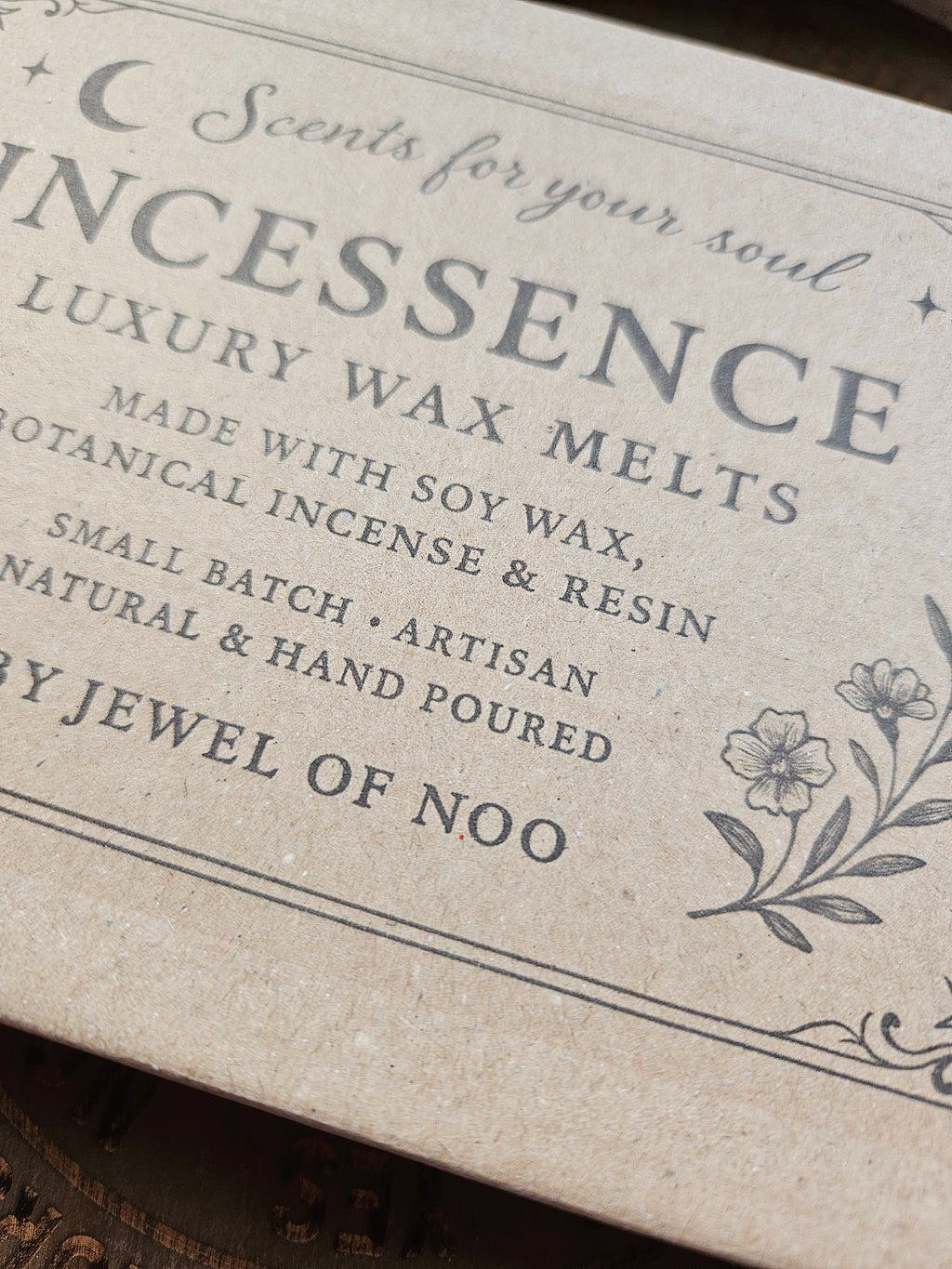 A close-up of a textured kraft paper box labeled 'INCESSENCE Luxury Wax Melts' with botanical illustrations and text including 'Small Batch Artisan Natural & Hand Poured' and 'Scent for your soul'.