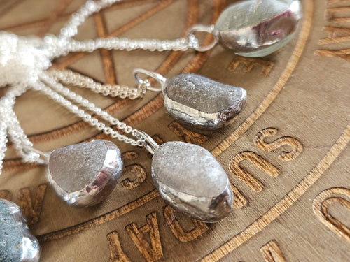 Silver necklace with pebble-like pendants on a wooden surface with engraved text.
