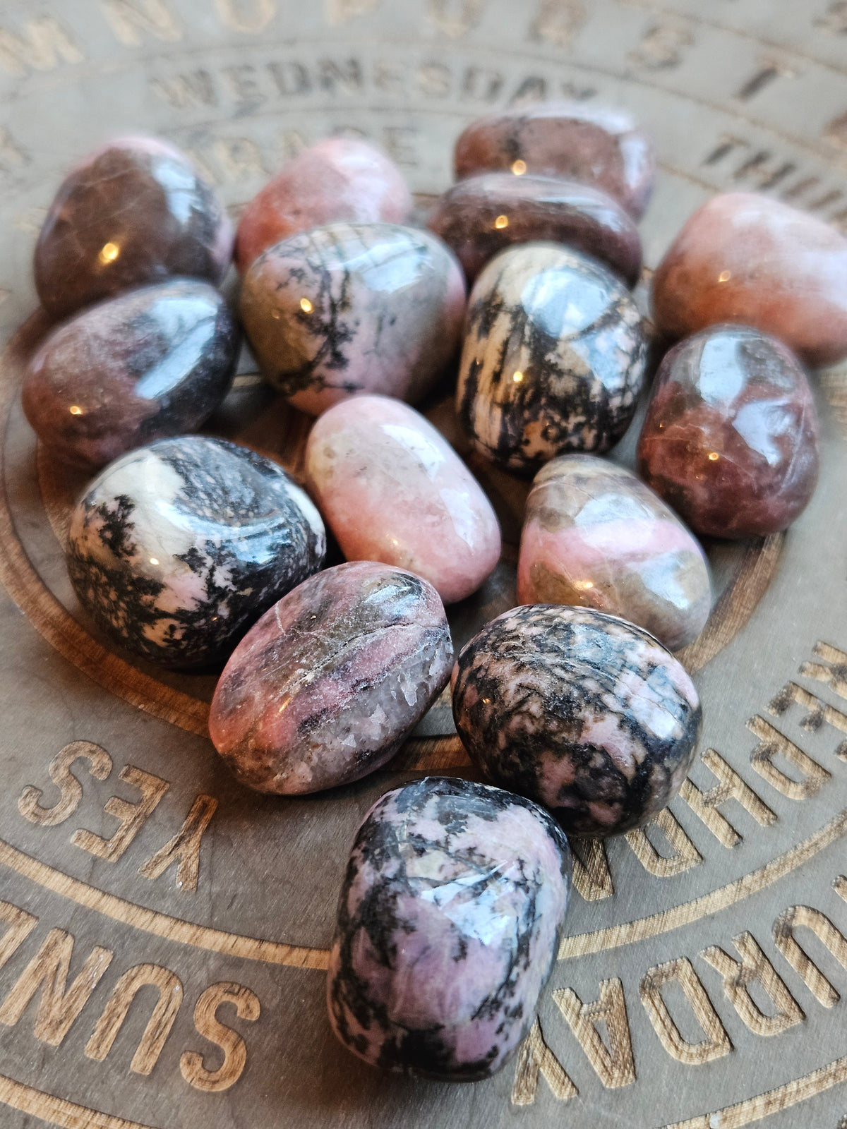 Pink and black Rhodonite tumble stones on a wooden board