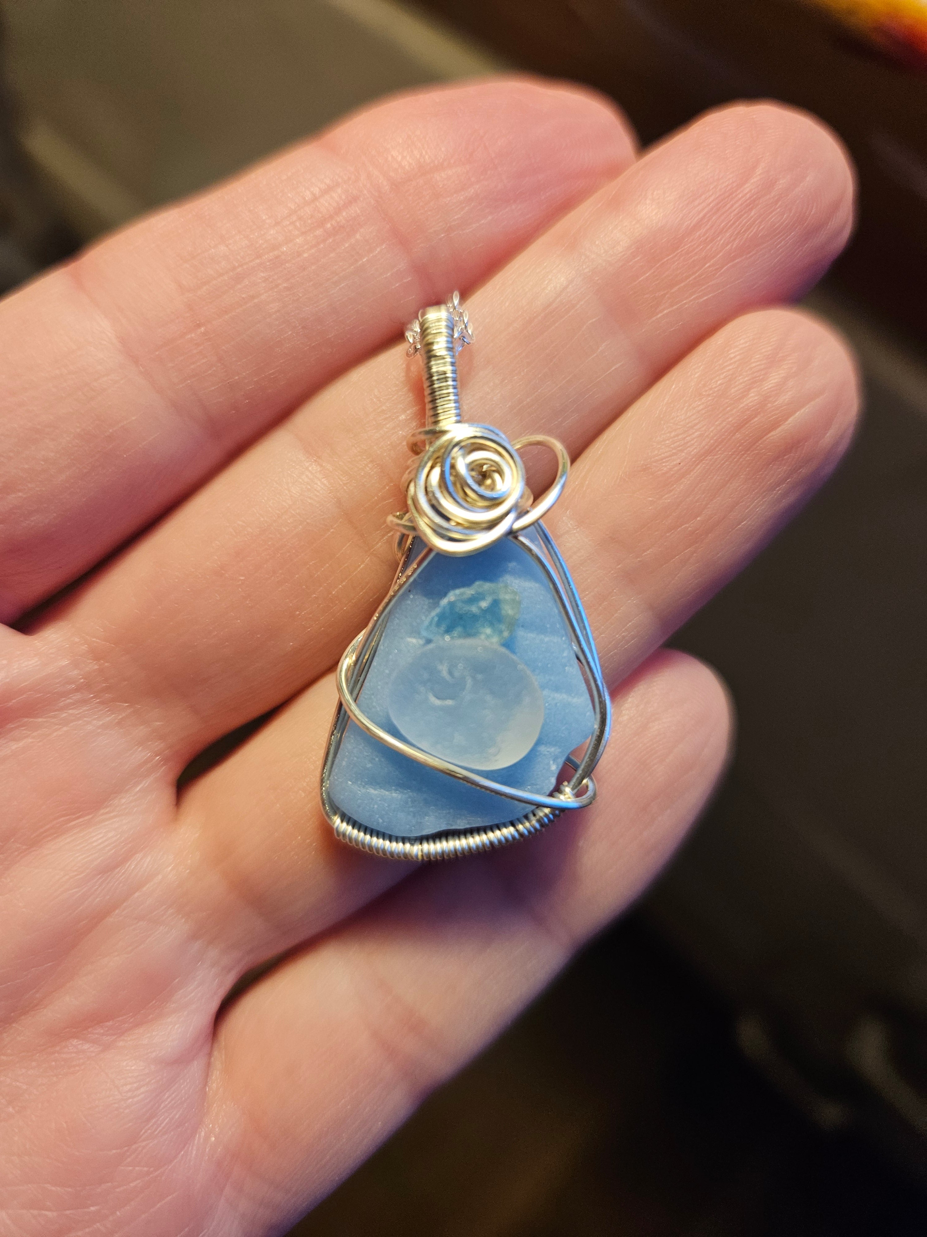 Hand holding a blue stone pendant with silver wire wrapping to show the size