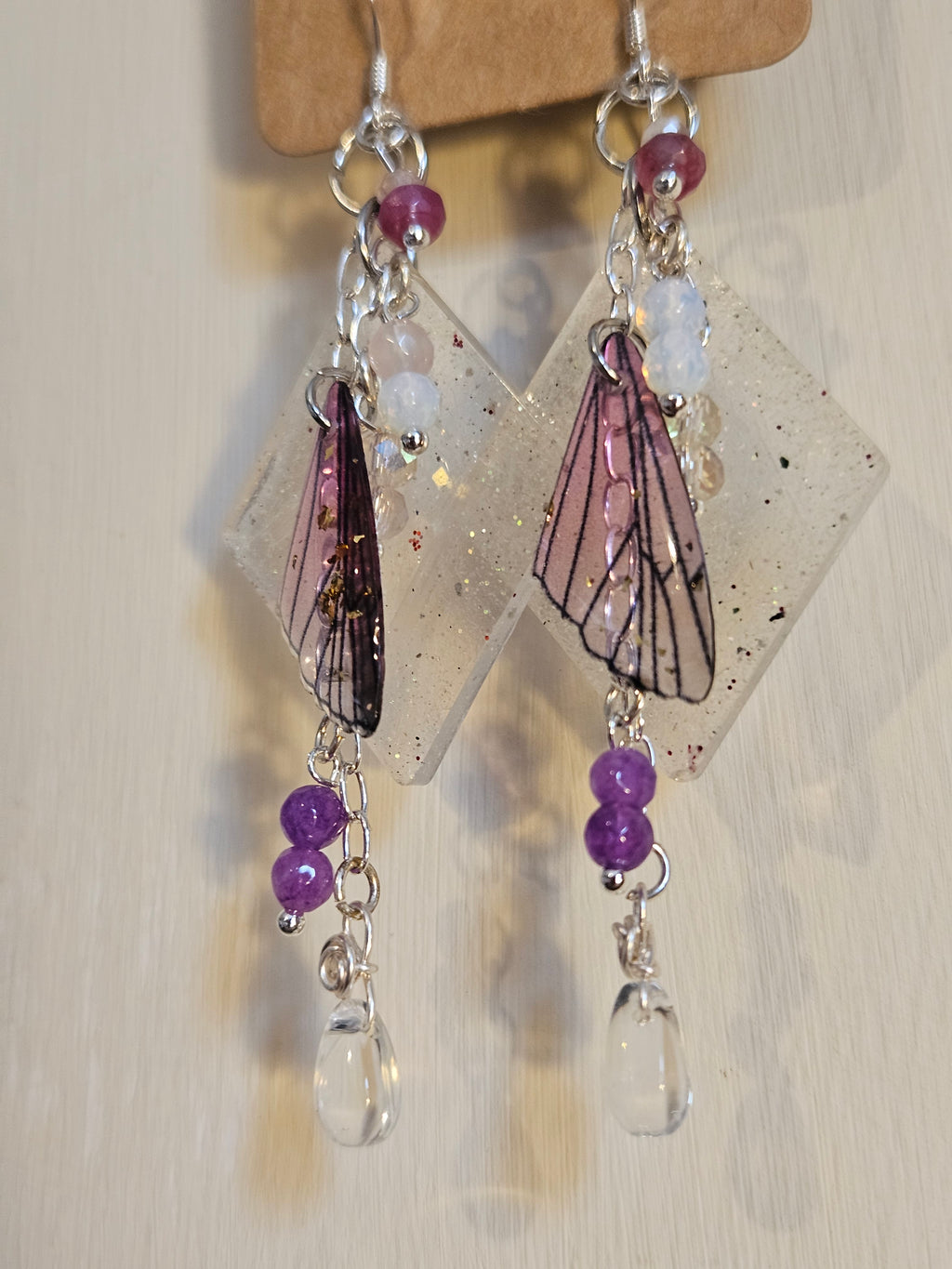 Decorative earrings with purple beads and butterfly wings on a light background