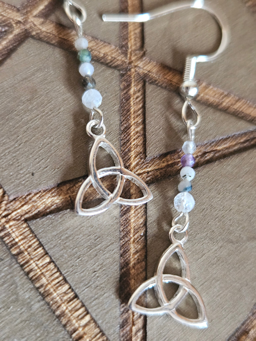 Silver Celtic knot earrings with beaded chain on a wooden surface