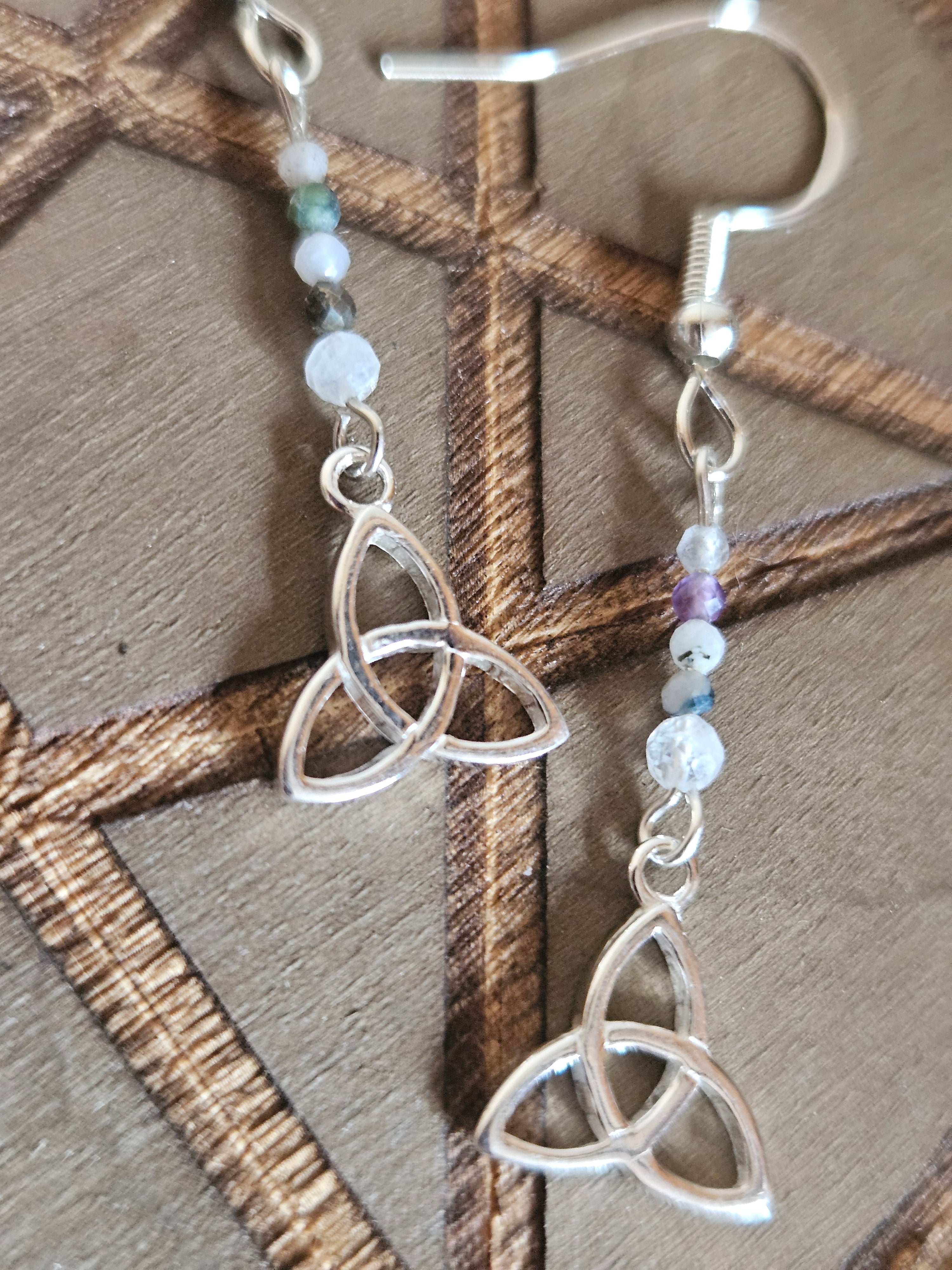 Silver Celtic knot earrings with beaded chain on a wooden surface