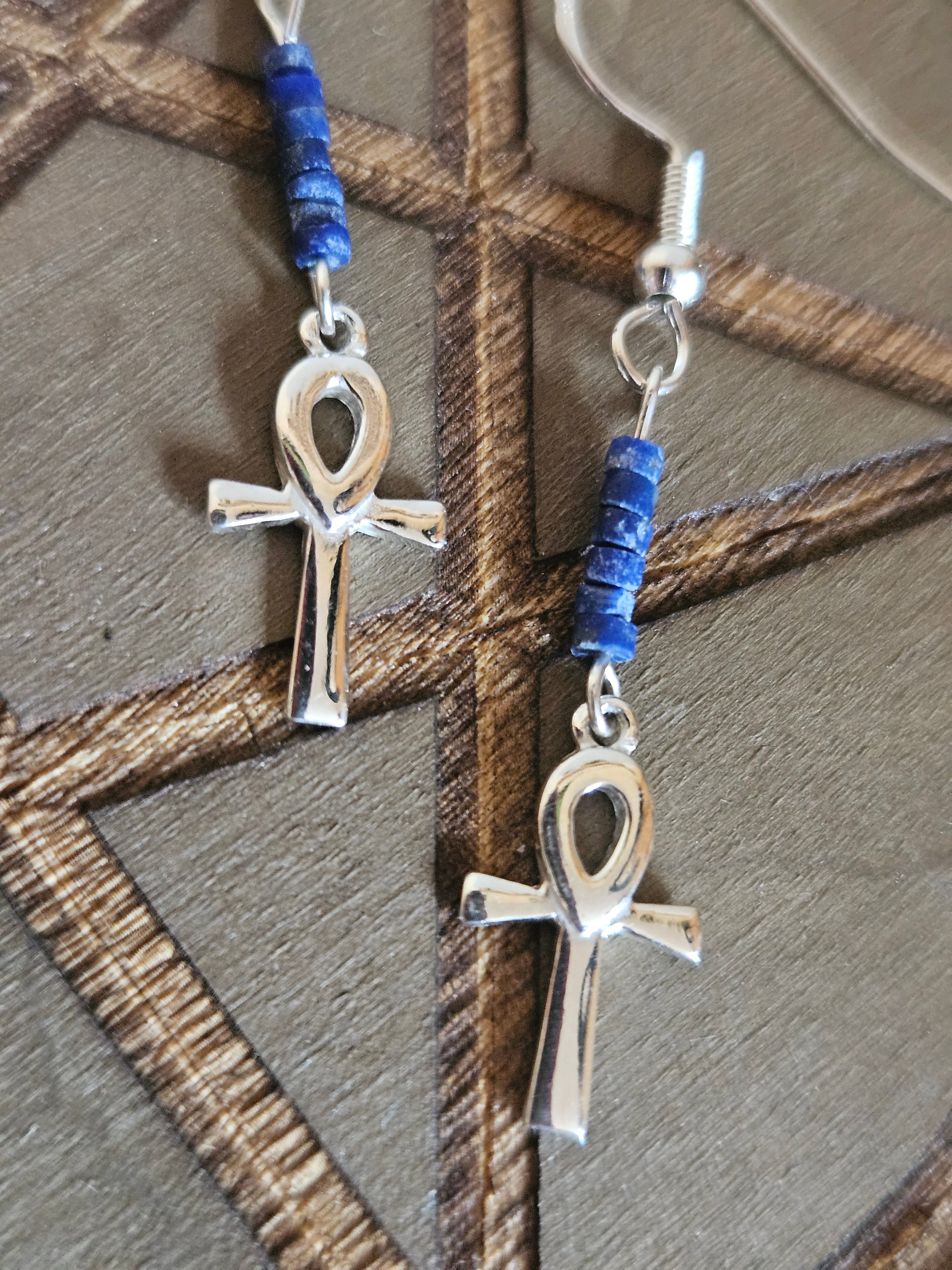 Silver ankh pendants with blue beads on a textured surface