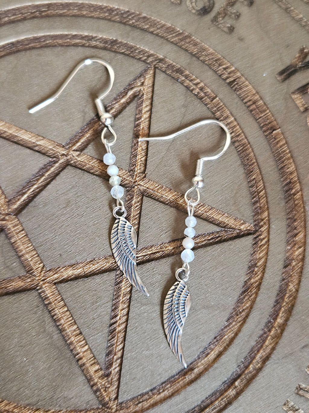 Silver winged earrings with beads on a pentagram design background