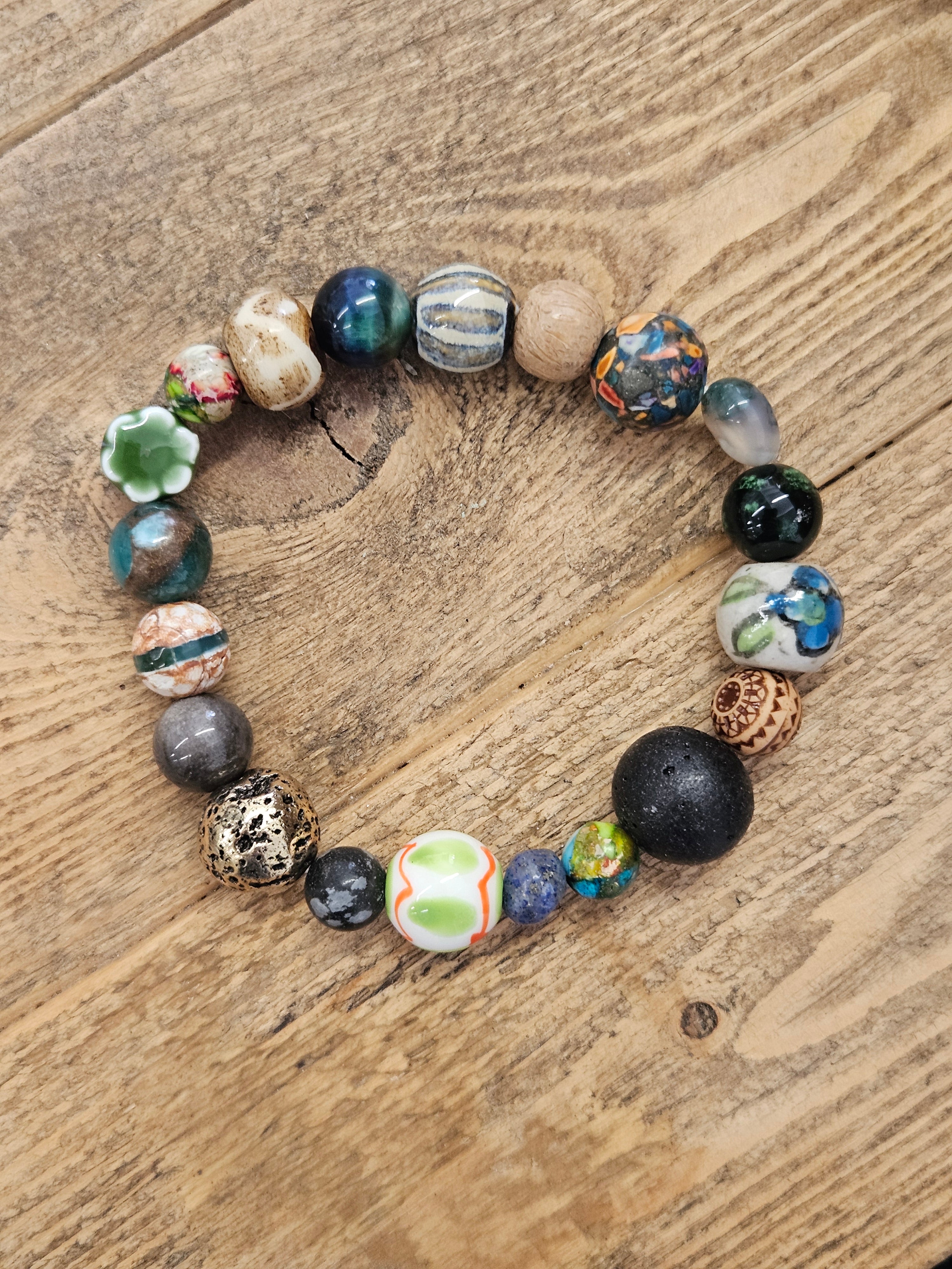 A beaded stretch bracelet with a variety of colorful, textured, and patterned glass beads, displayed on a rustic wooden surface.