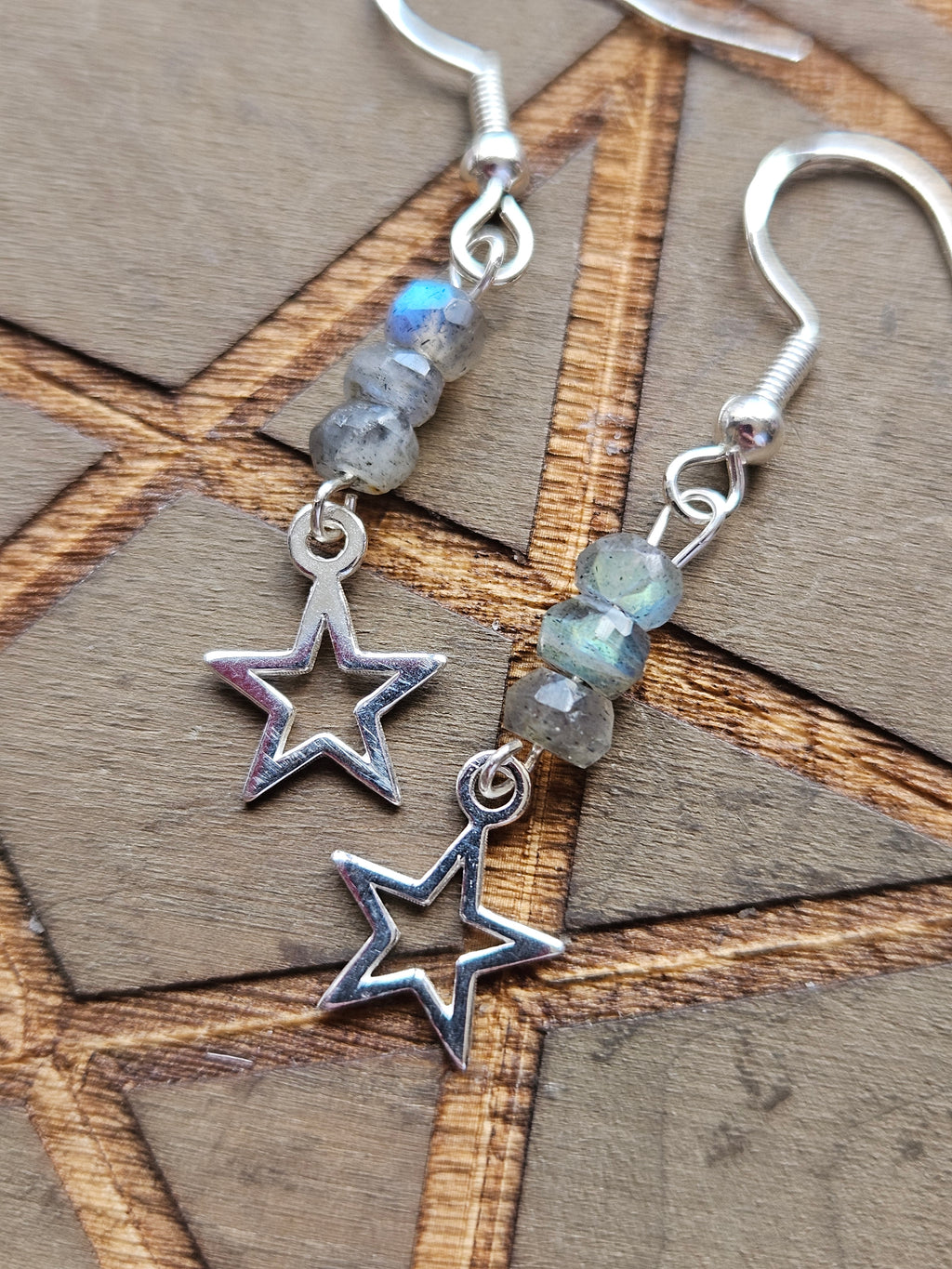 Silver dangle earrings with open star-shaped charms and faceted gray-blue labradorite beads, displayed on a wooden surface.