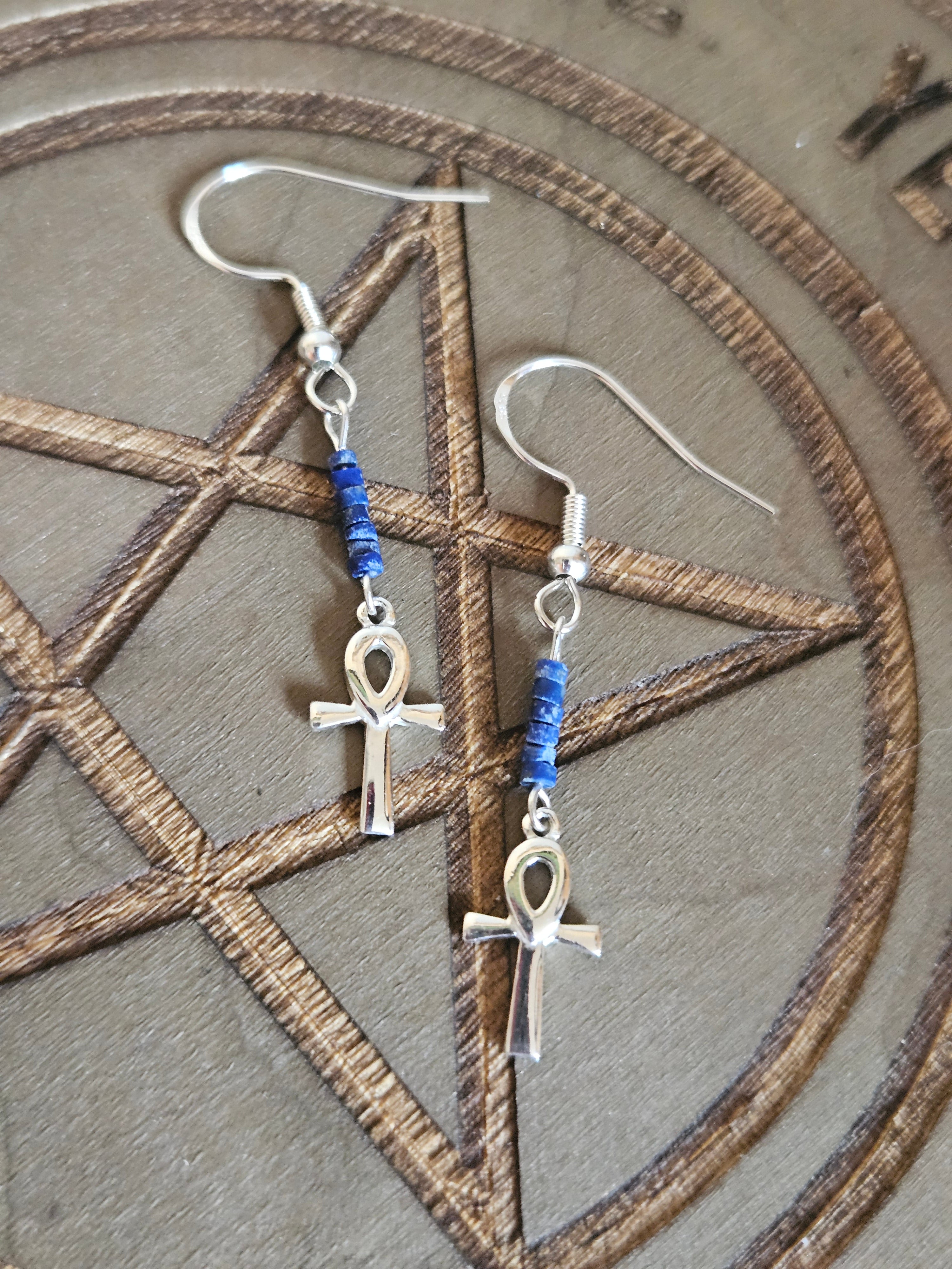 Pair of ankh shaped earrings with blue beads on a pentagram design background