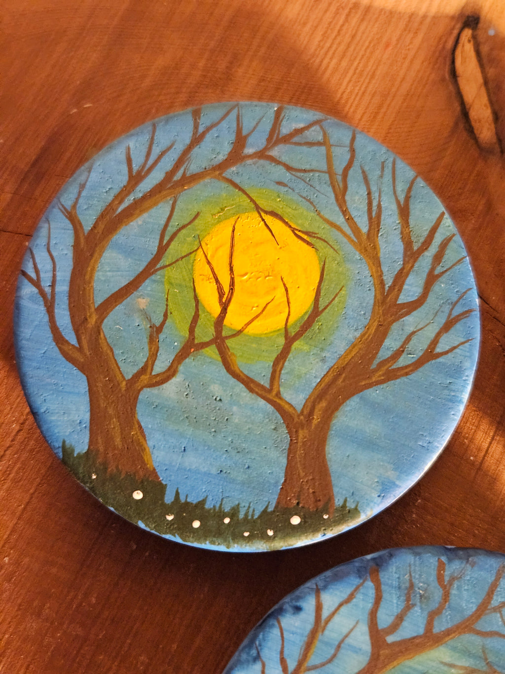 Round painted magnet with tree branches and a sun on a wooden surface