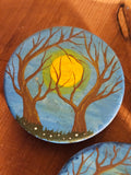 Round painted magnet with tree branches and a sun on a wooden surface