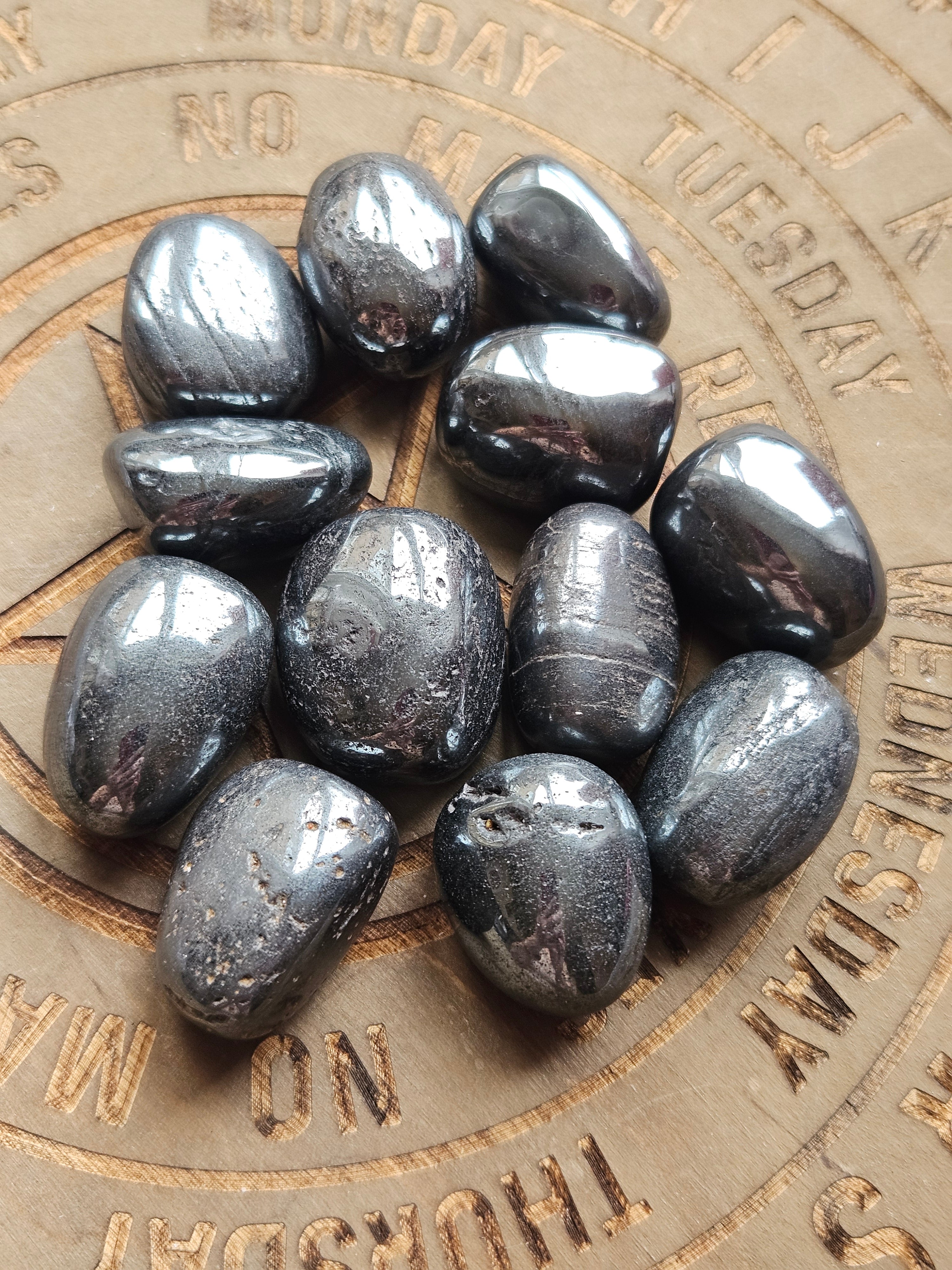 A pile of polished grey gemstone tumbles, Hematite, resting on a wooden circular calendar coaster.