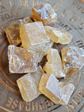 A pile of rough, translucent yellow gemstone chunks resting on a circular wooden tray with engraved text.