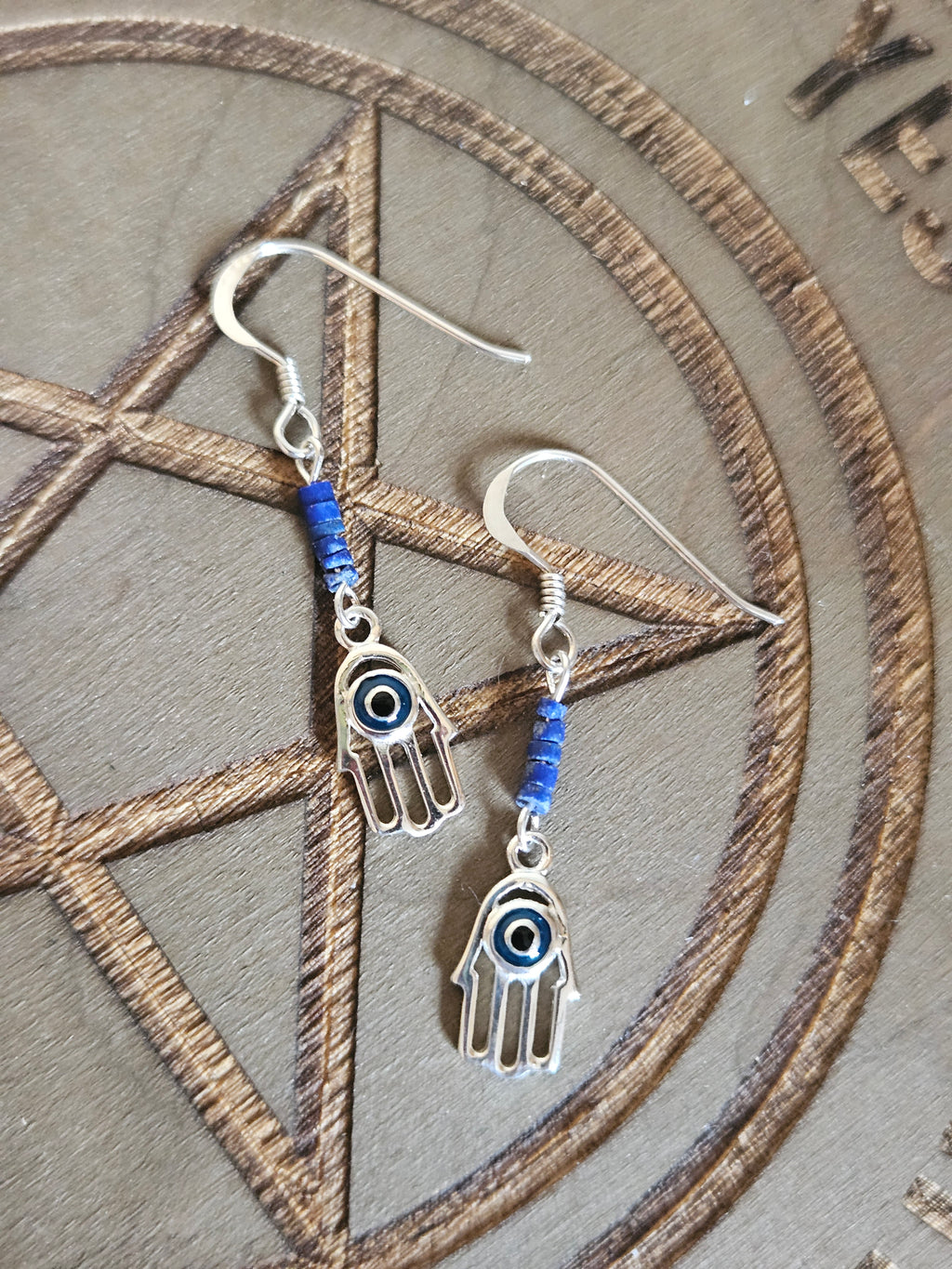 Silver hand-shaped earrings with blue beads on a pentagram design background