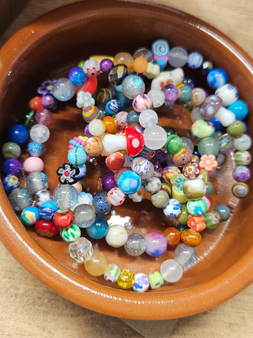 Colorful beaded bracelets in a terracotta pot on a wooden surface