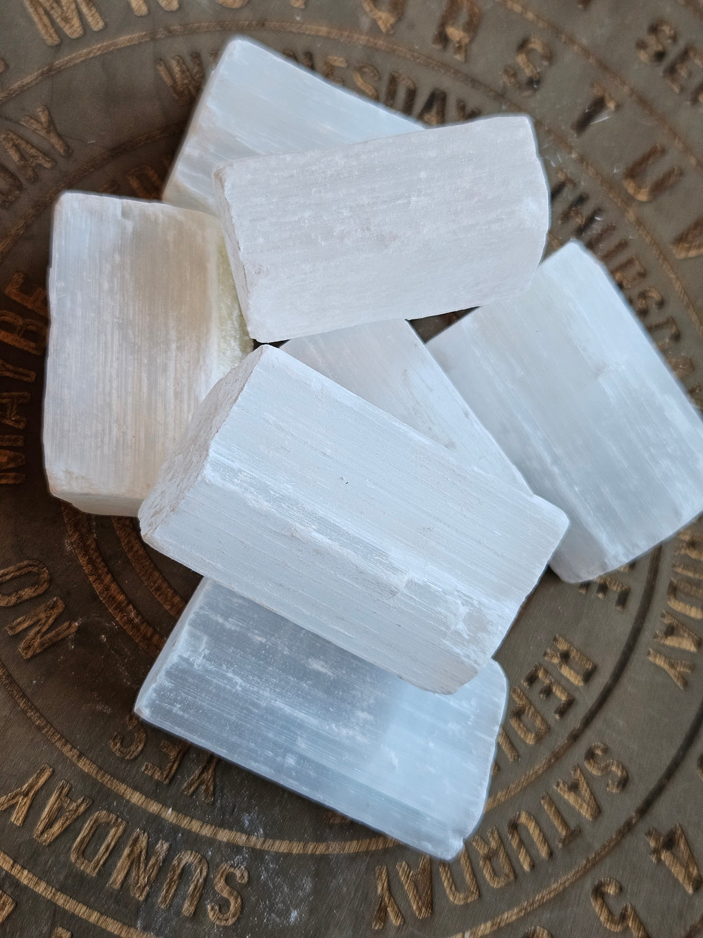 Five white selenite crystal chunks arranged on a round bronze-toned metal plate with engraved days of the week.