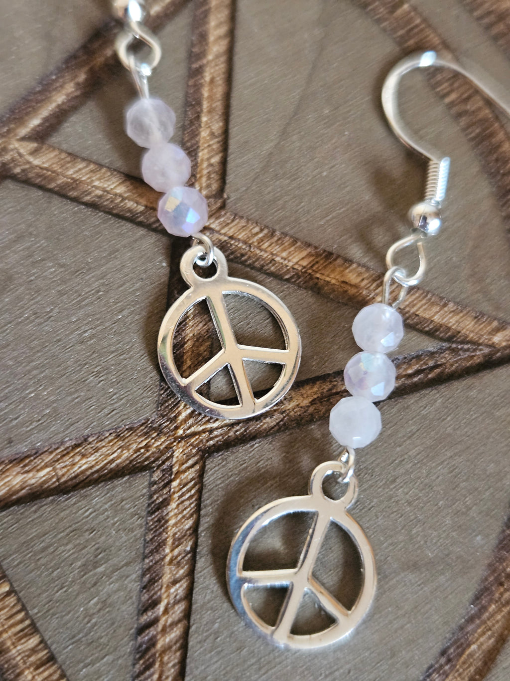 Silver peace symbol earrings with beaded chain on a wooden surface
