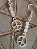 Silver peace symbol earrings with beaded chain on a wooden surface