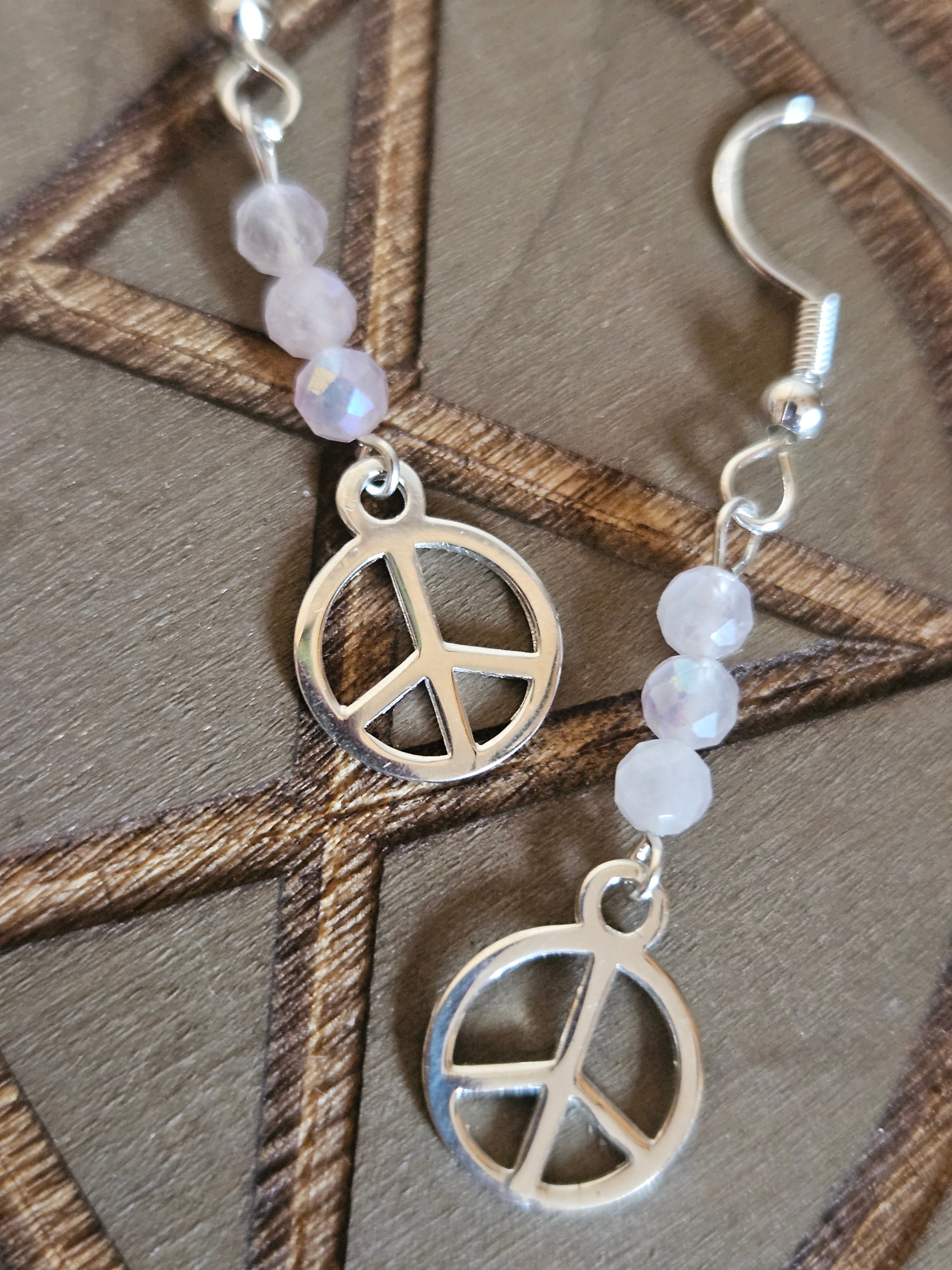 Silver peace symbol earrings with beaded chain on a wooden surface