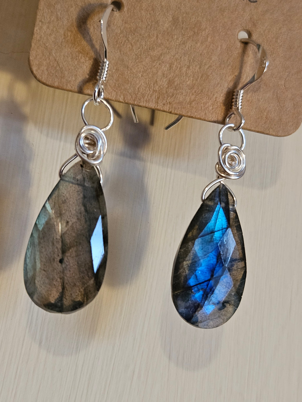 Teardrop-shaped Labradorite earrings on a light brown card with a neutral background