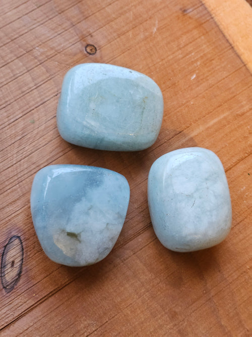 Three light blue Aquamarine stones on a wooden surface