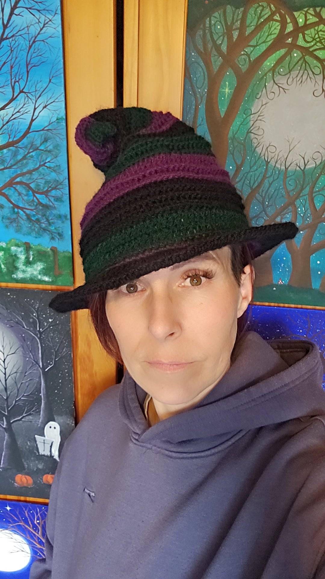 Person wearing a striped hat and hoodie in front of a decorative wall with tree designs.